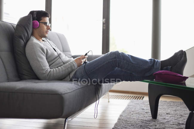 Homem ouvindo música com MP3 player no sofá na sala de estar — Fotografia de Stock