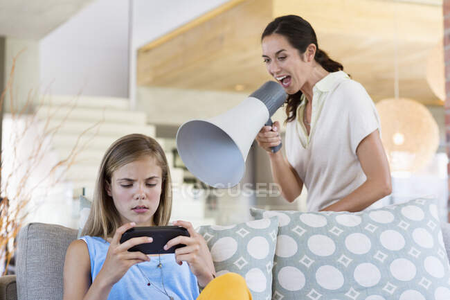 Woman shouting through a megaphone at his daughter for playing video game — Stock Photo
