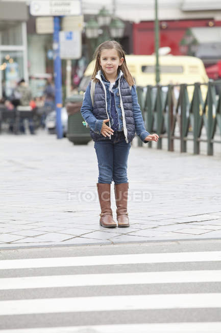 Smiling little schoolgirl standing at roadside in city — Stock Photo