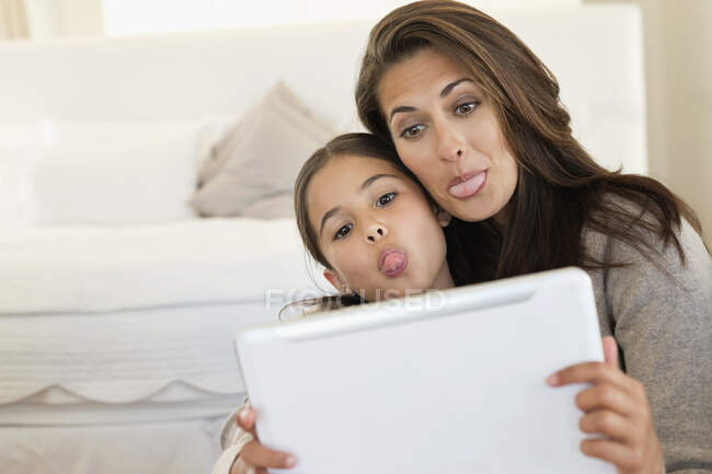 Mujer y su hija haciendo sus caras delante de la tableta digital - foto de stock