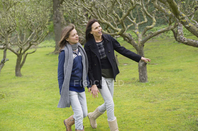 Femme avec fille adolescente marchant dans le verger — Photo de stock