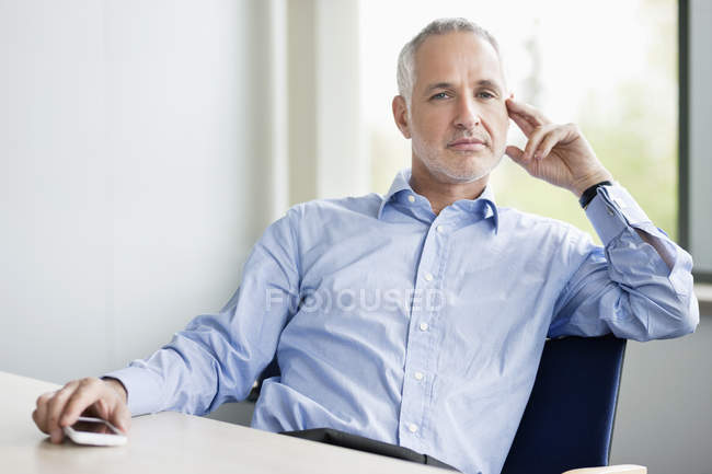 Homme d'affaires confiant assis dans le bureau et regardant la caméra — Photo de stock