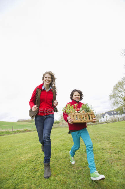 Niño llevando una cesta de verduras variadas con su madre en una granja - foto de stock