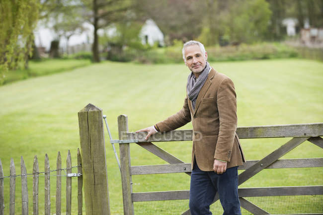 Portrait of elegant man standing at wooden fence in park — Stock Photo