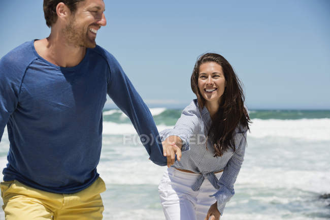 Fröhliches Paar läuft Händchen haltend am Strand — Stockfoto