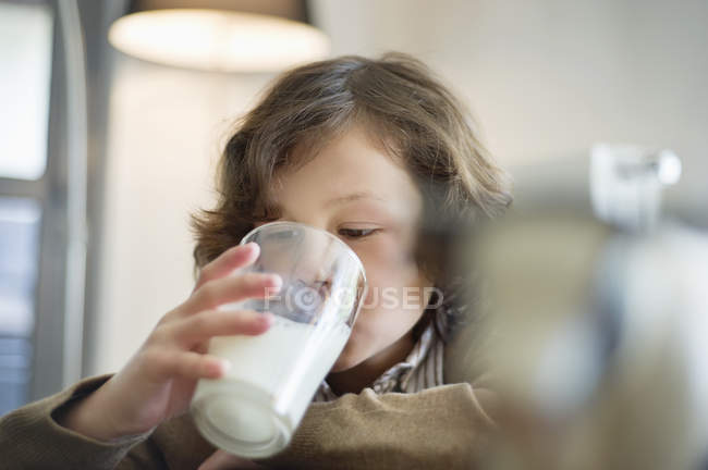 Primer plano del niño bebiendo leche de vidrio en la cocina - foto de stock