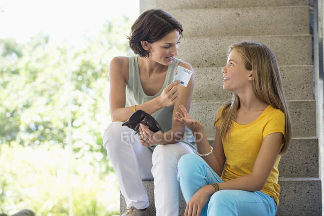 Mujer dando dinero de bolsillo a su hija - foto de stock