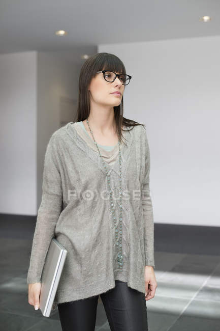 Уверенная молодая деловая женщина, держащая ноутбук и стоящая в офисе — стоковое фото