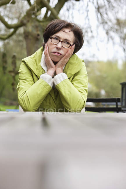 Уставшая вдумчивая женщина, опирающаяся на локти за столом на открытом воздухе — стоковое фото