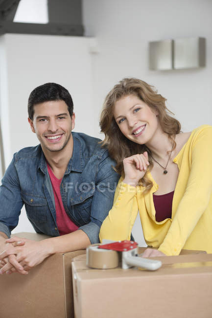 Улыбающаяся пара наклоняется над картонными коробками в квартире и смотрит в камеру — стоковое фото