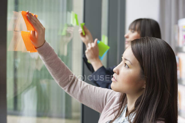 Empresárias colando notas de memorando em vidro em um escritório — Fotografia de Stock