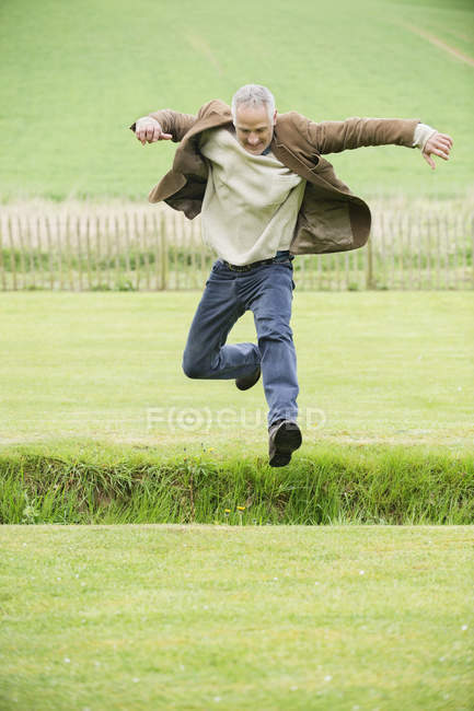 Веселый взрослый мужчина прыгает в зеленое поле — стоковое фото
