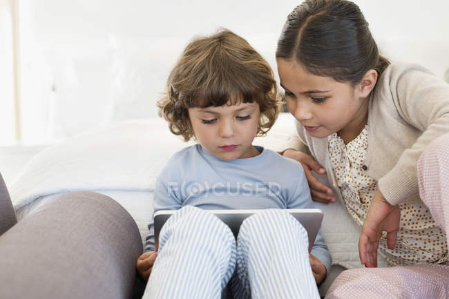 Menina olhando para o irmão usando tablet digital em casa — Fotografia de Stock