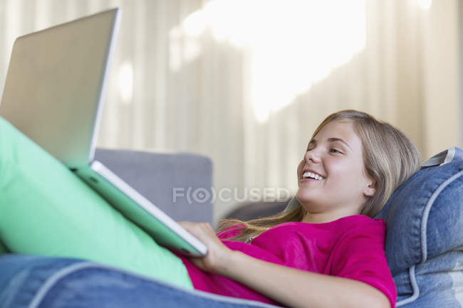 Дівчина лежить на бобовій сумці і використовує ноутбук — стокове фото