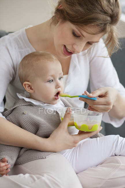 Woman feeding baby daughter at home — Stock Photo