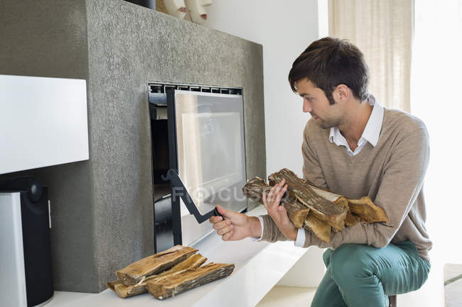 Man putting firewood into fireplace in apartment — Stock Photo