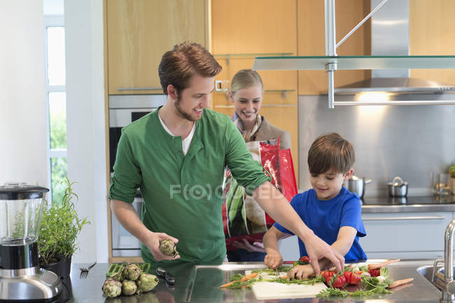 Родители смотрят, как сын режет овощи на кухне — стоковое фото