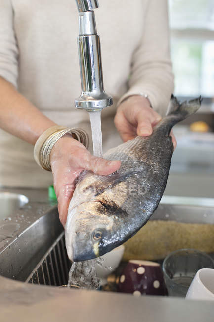 Gros plan des mains féminines qui lavent le poisson dans l'évier de cuisine — Photo de stock