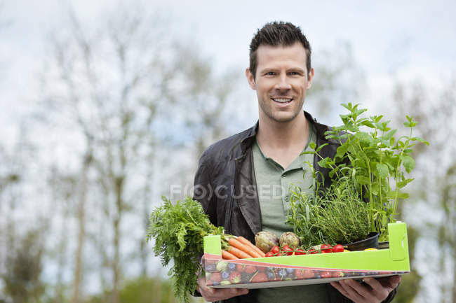 Portrait of man holding tray of raw vegetables outdoors — Stock Photo