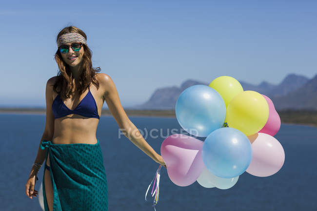 Mujer elegante feliz sosteniendo globos contra el cielo azul - foto de stock
