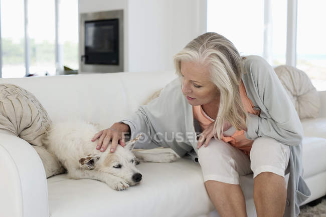 Frau sitzt zu Hause auf Couch und streichelt Hund — Stockfoto