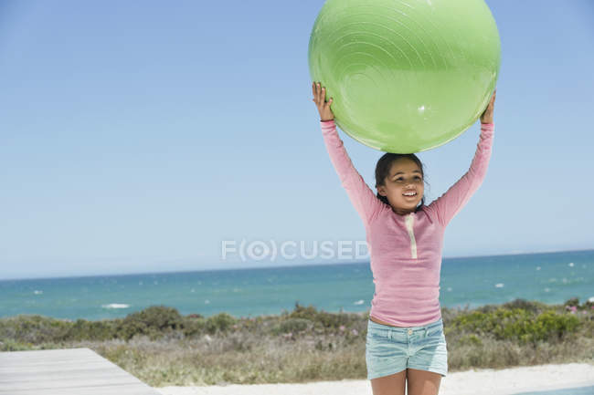 Smiling little girl holding fitness ball on beach — Stock Photo