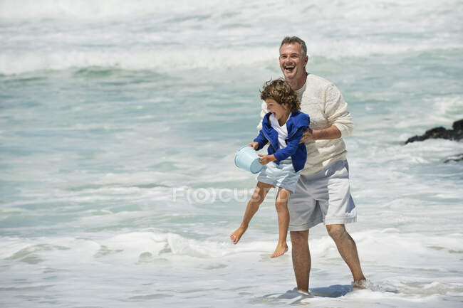 Boy playing with his grandfather on the beach — Stock Photo