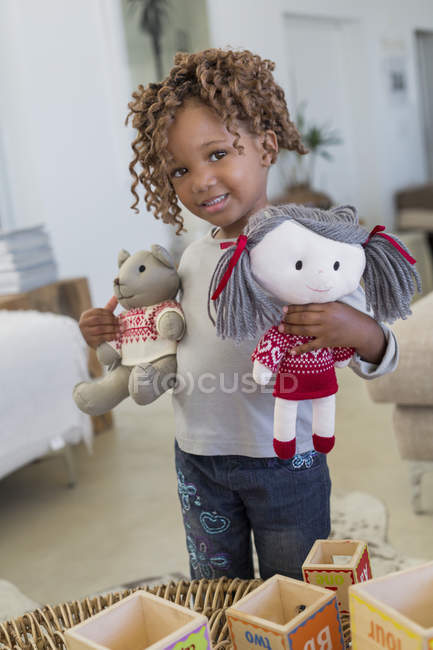 Portrait of little girl standing with dolls in room — Stock Photo