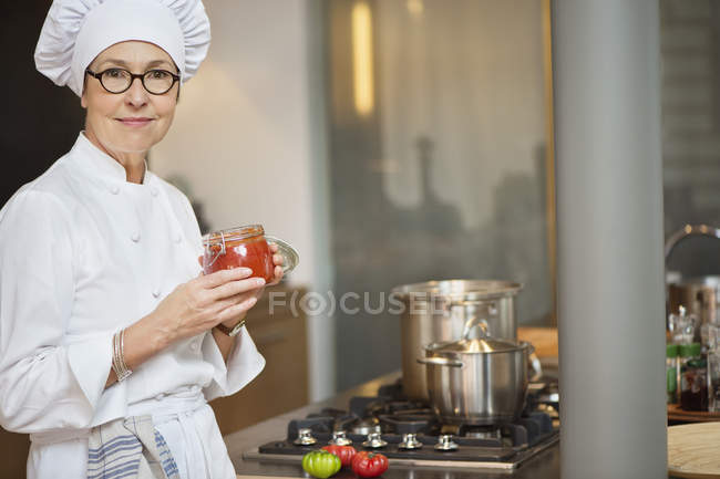 Portrait de femme en costume de chef tenant un pot de sauce tomate — Photo de stock