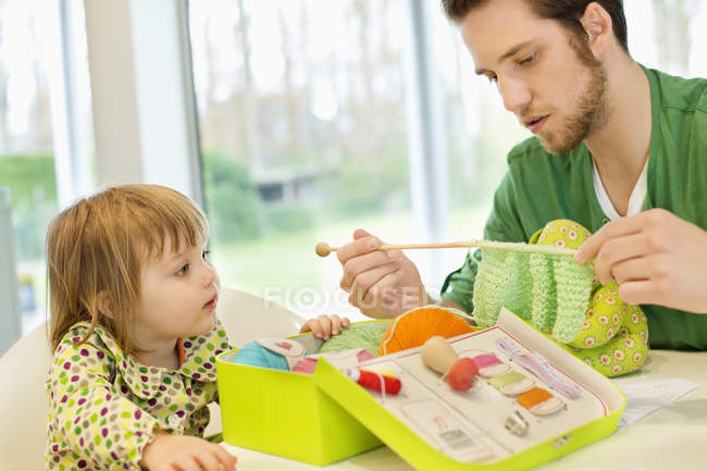 Girl looking at father knitting with wool at home — Stock Photo