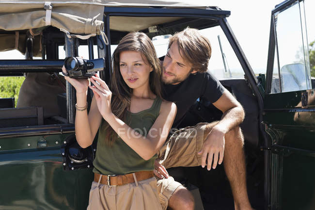 Femme avec petit ami filmant avec caméra vidéo devant un van ouvert — Photo de stock