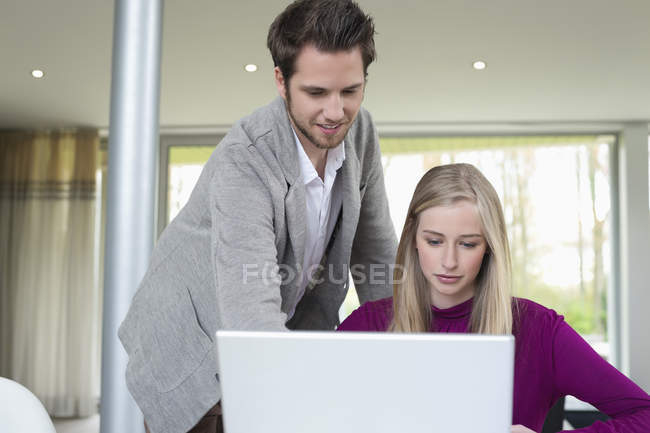Mulher trabalhando no laptop com homem ajudando no escritório — Fotografia de Stock