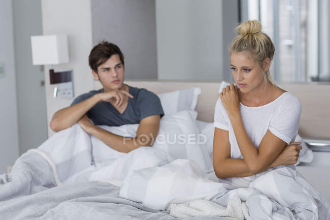 Jovem casal sentado na cama com dificuldades de relacionamento — Fotografia de Stock