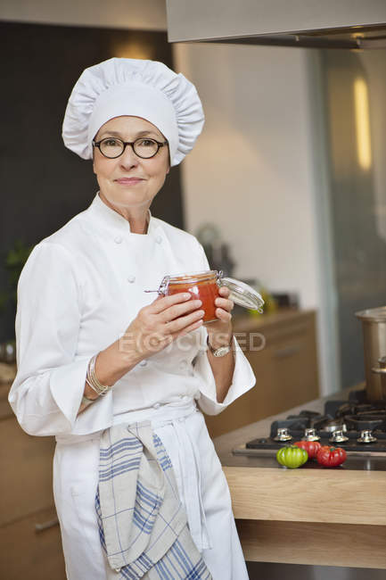 Portrait de femme en costume de chef tenant un pot de sauce tomate — Photo de stock