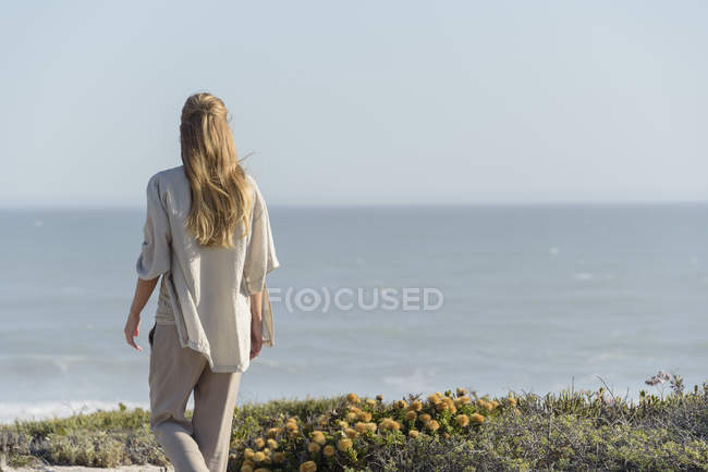 Rückansicht einer Frau, die am Strand steht und die Aussicht betrachtet — Stockfoto