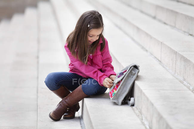 Kleines Mädchen öffnet Schulranzen auf Treppe im Freien — Stockfoto