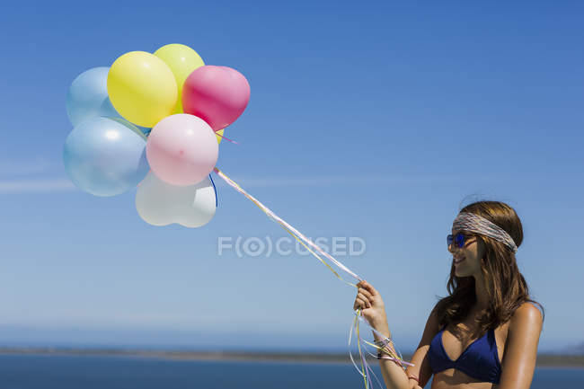 Primer plano de la mujer con estilo feliz sosteniendo globos contra el cielo azul - foto de stock