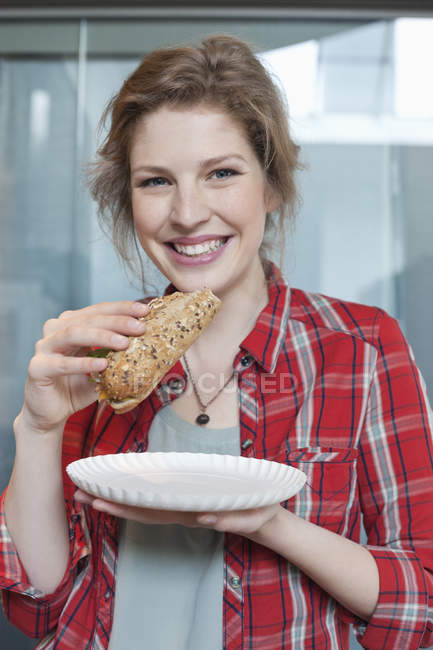 Портрет усміхненої молодої жінки, що їсть бутерброд — стокове фото