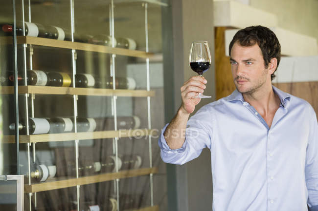 Homme regardant du vin rouge dans un verre à vin — Photo de stock