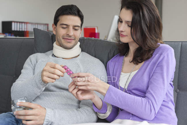 Woman giving medicine to husband suffering from neck ache — Stock Photo