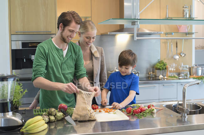 Батьки дивляться на сина, який ріже овочі на кухні — стокове фото