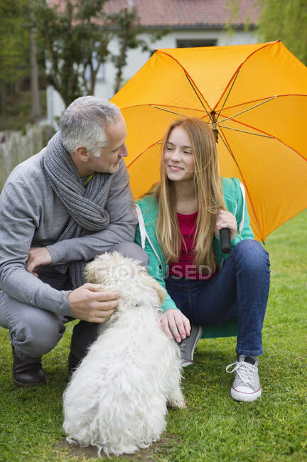 Homme avec sa fille choyer un chien dans une pelouse — Photo de stock