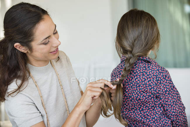 Mujer sonriente trenzando el cabello de su hija - foto de stock