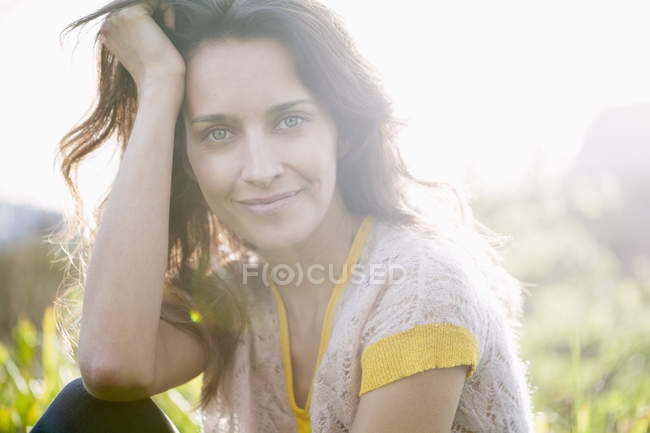 Sonriente mujer en la naturaleza soleada sosteniendo pequeña flor de margarita - foto de stock