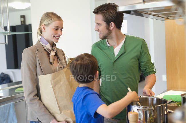 Hombre e hijo cocinando comida para la madre después de comprar - foto de stock