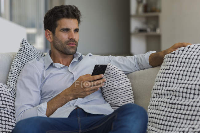 Mann sitzt auf Couch und hält Smartphone in der Hand — Stockfoto