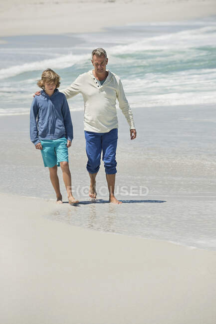 Homem caminhando com seu neto na praia — Fotografia de Stock