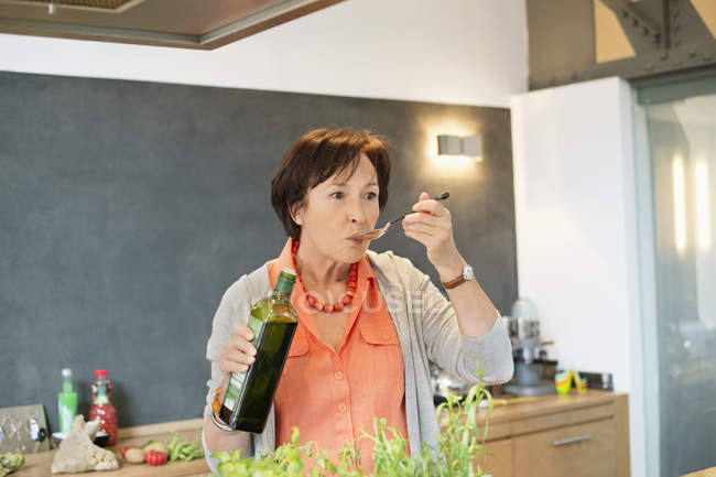 Seniorin verkostet Olivenöl in Küche — Stockfoto