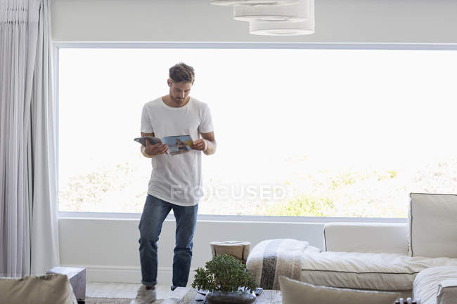 Joven hombre guapo leyendo revista en la sala de estar en casa - foto de stock