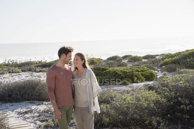Happy couple walking in vegetation on sea coast — Stock Photo